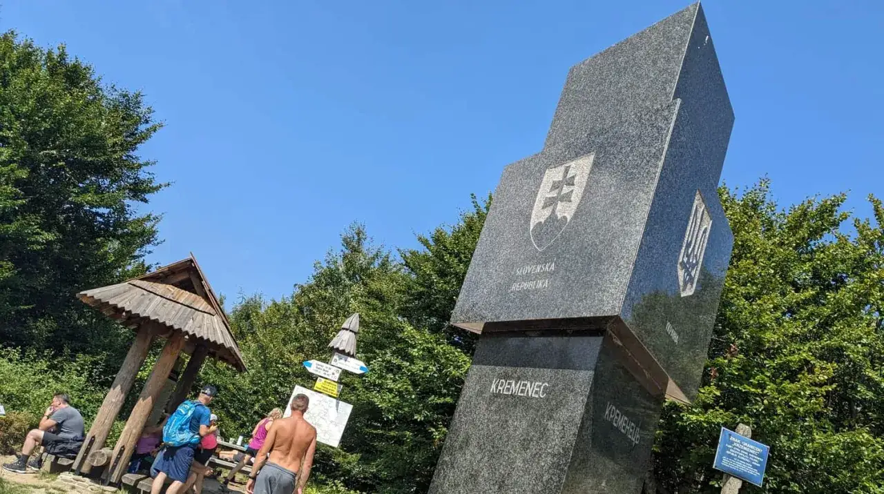 Trójstyk granic Bieszczady: monument z herbami Słowacji i Ukrainy, drewniana wiata i turyści.