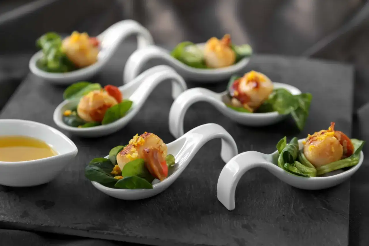 Délicieuses saint jacques au barbecue, servies sur des cuillères blanches avec des feuilles vertes et une touche de tomate. Un délice à savourer !