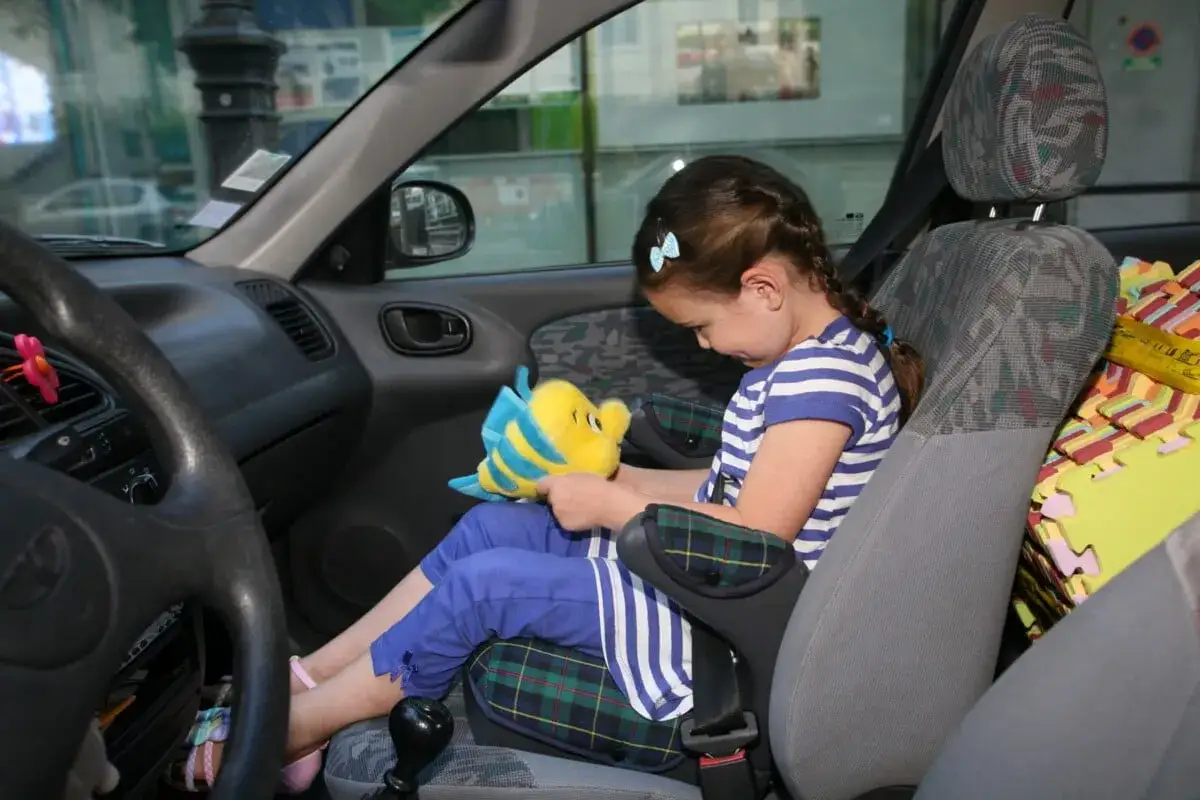 Une petite fille, trop jeune pour monter devant en voiture, joue avec une peluche dans son siège auto.