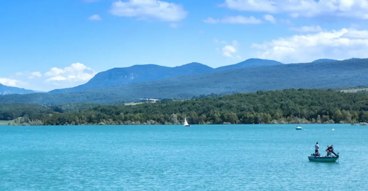 Le lac de Montbel, un voilier et un bateau de pêche sous un ciel bleu.