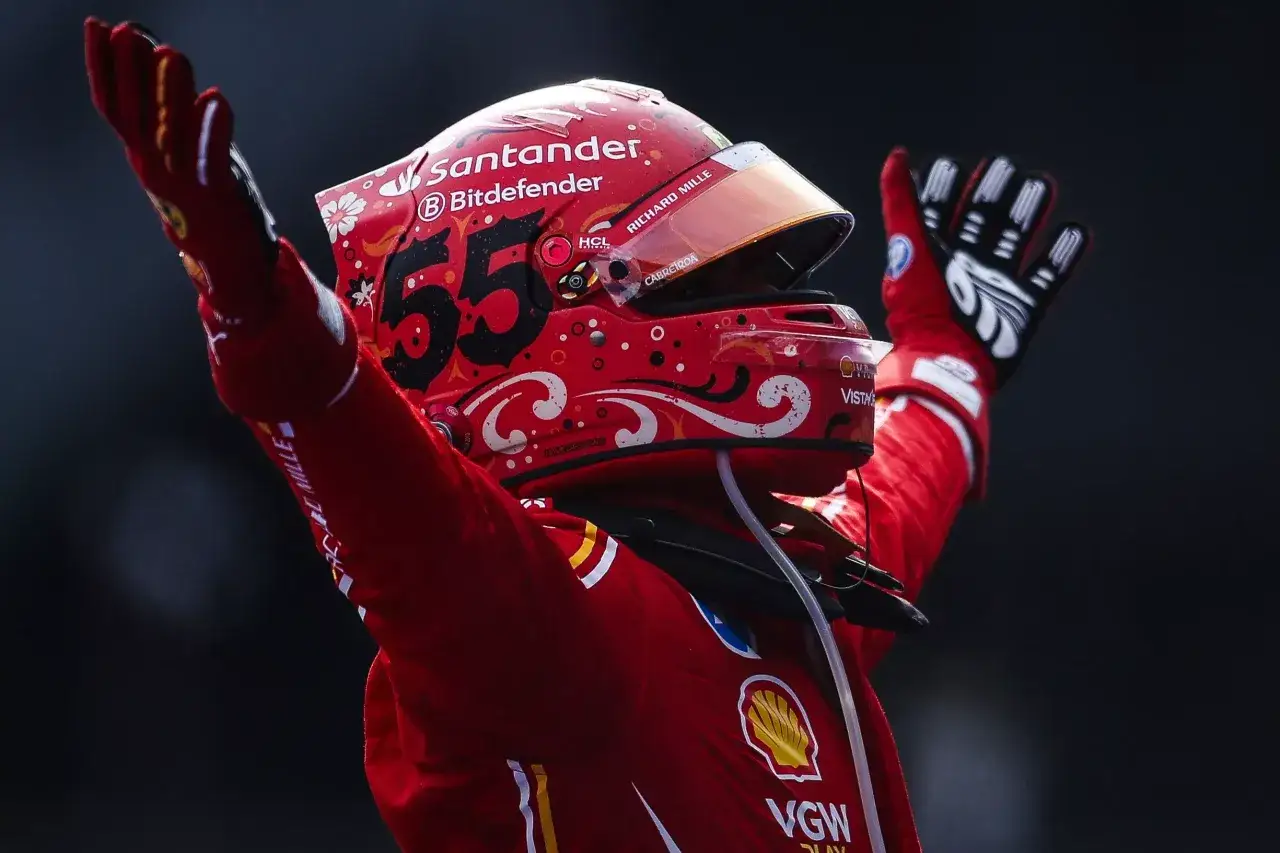 Carlos Sainz, piloto de Ferrari, celebra con los brazos en alto. Su casco rojo lleva el n&uacute;mero 55 y decoraciones florales.