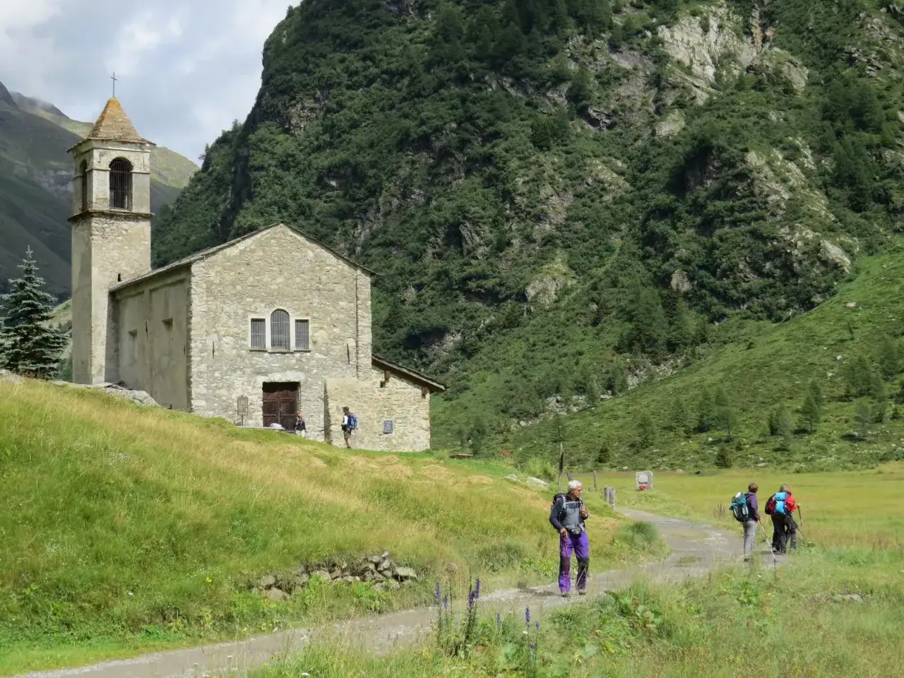 Chiesa in pietra in Val di Rezzalo, con escursionisti su un sentiero. Come arrivare: segui il sentiero panoramico.
