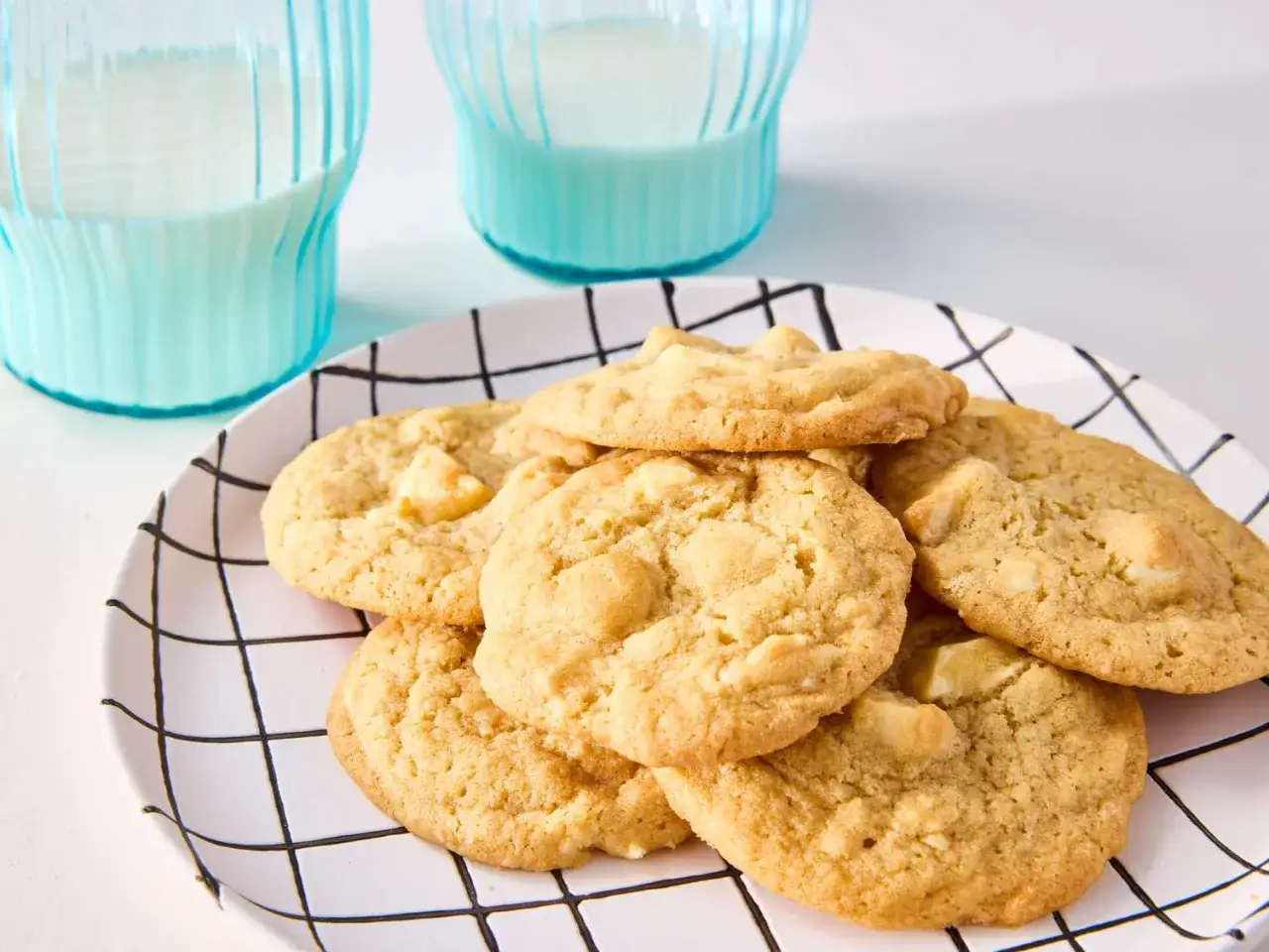 Ein Teller mit saftigen white chocolate macadamia cookies, daneben zwei Gläser Milch.