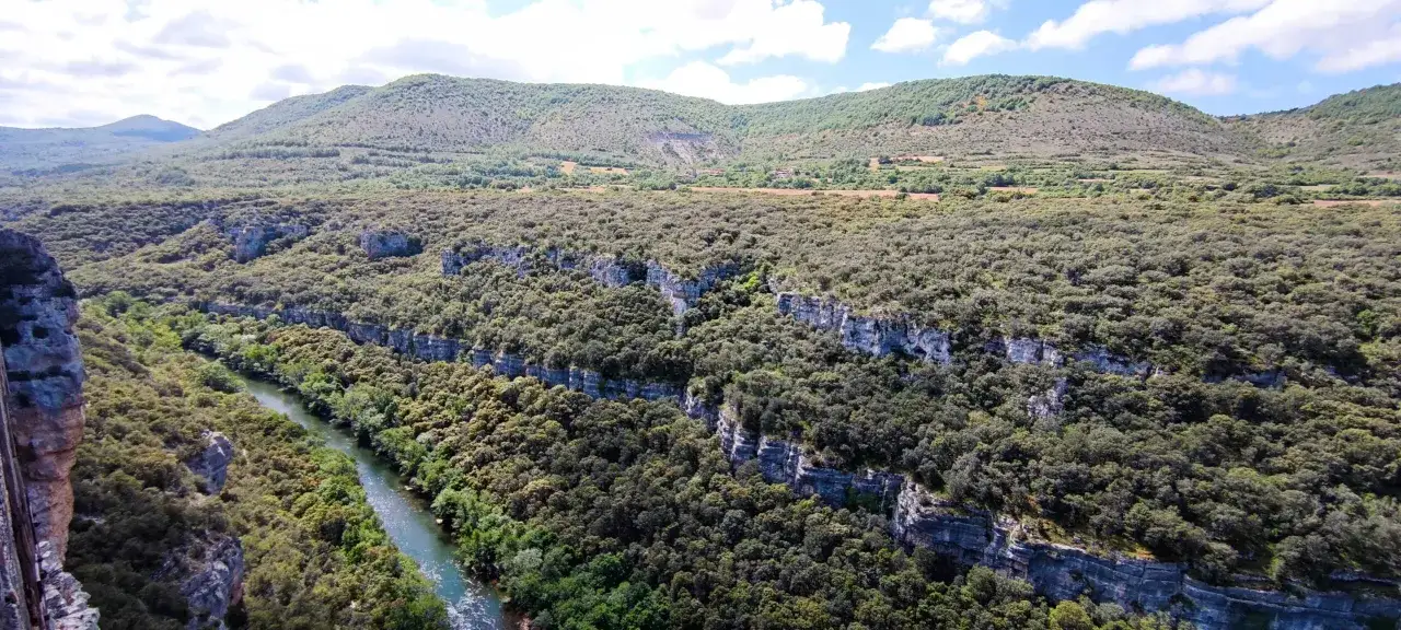 Un r&iacute;o serpentea entre ca&ntilde;ones boscosos, con acantilados rocosos que marcan el paisaje. Las **gr 99 etapas** de la naturaleza se despliegan ante la vista.