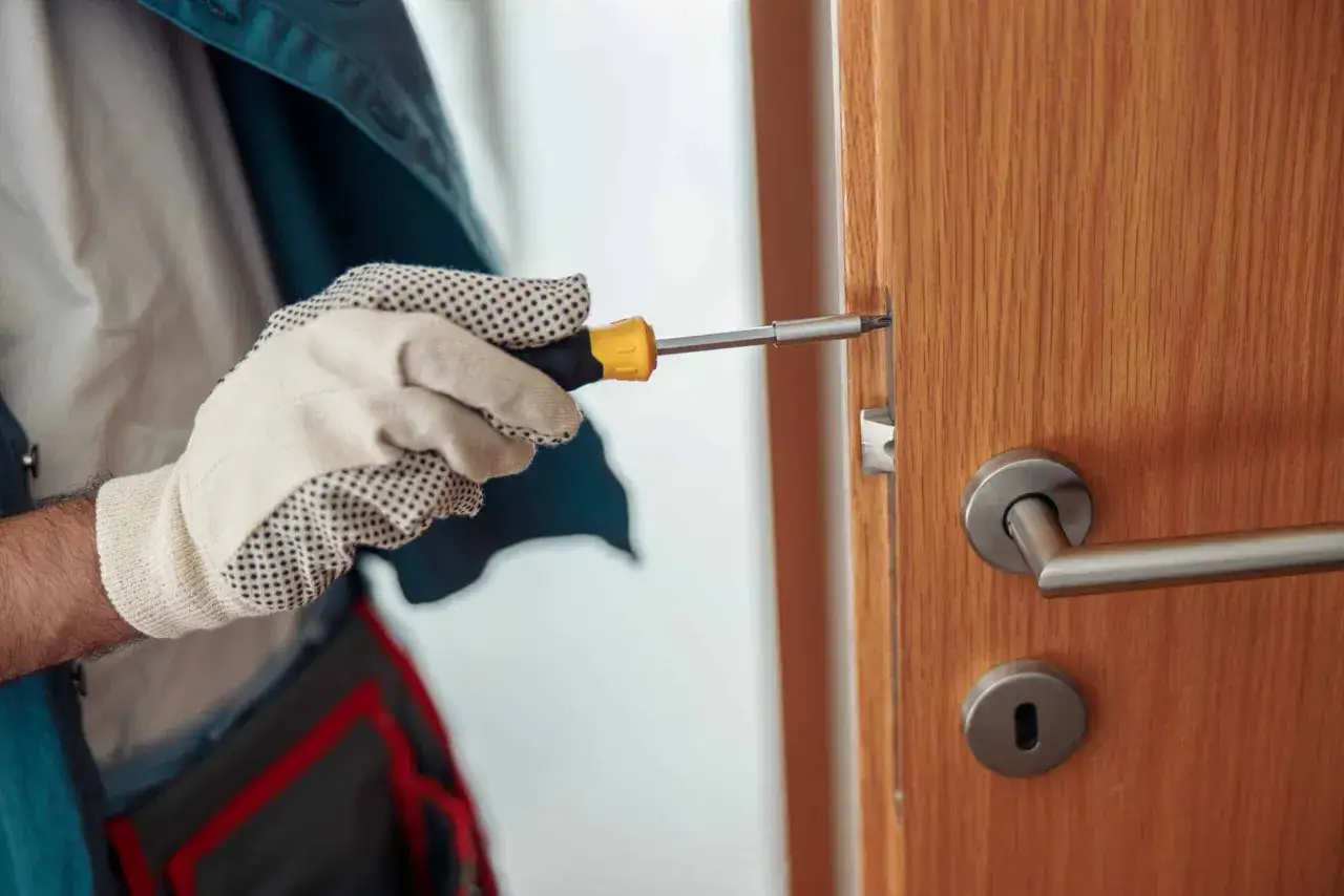 Main tenant utilise un tournevis pour réparer une serrure qui coince sur une porte en bois.