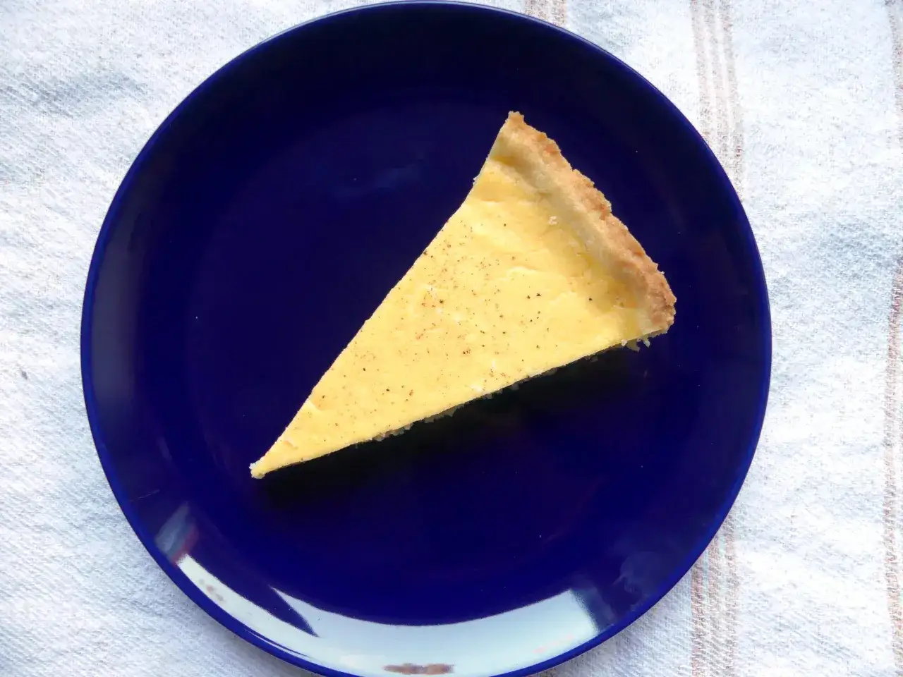 Ein St&uuml;ck Torta della Nonna, ein cremiger Kuchen mit Zitronengeschmack, auf einem blauen Teller.