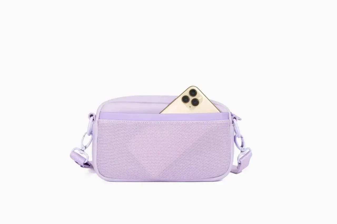 Packshot photo d'un sac bandoulière lilas avec une poche extérieure en filet. Un smartphone doré est glissé dans la poche.