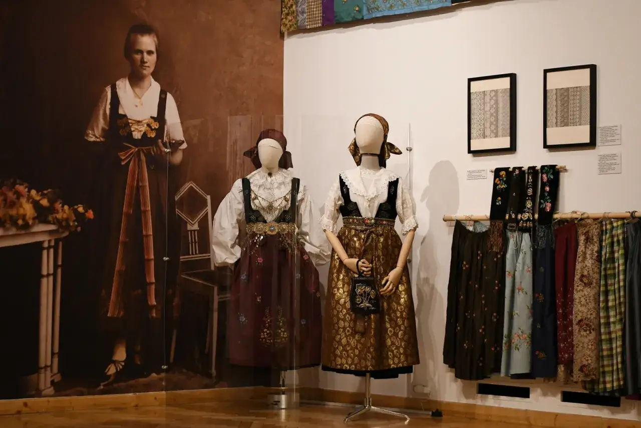W muzeum polskiej sztuki ludowej prezentowane są tradycyjne stroje. Dwie manekiny ubrane w barwne ludowe sukienki, obok wieszak z haftowanymi sp&oacute;dnicami.
