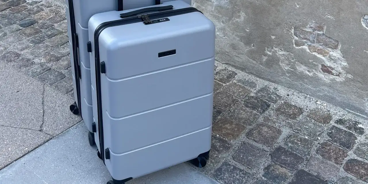 Två grå resväskor, perfekta som jettime handbagage, står på en kullerstensbelagd trottoar.
