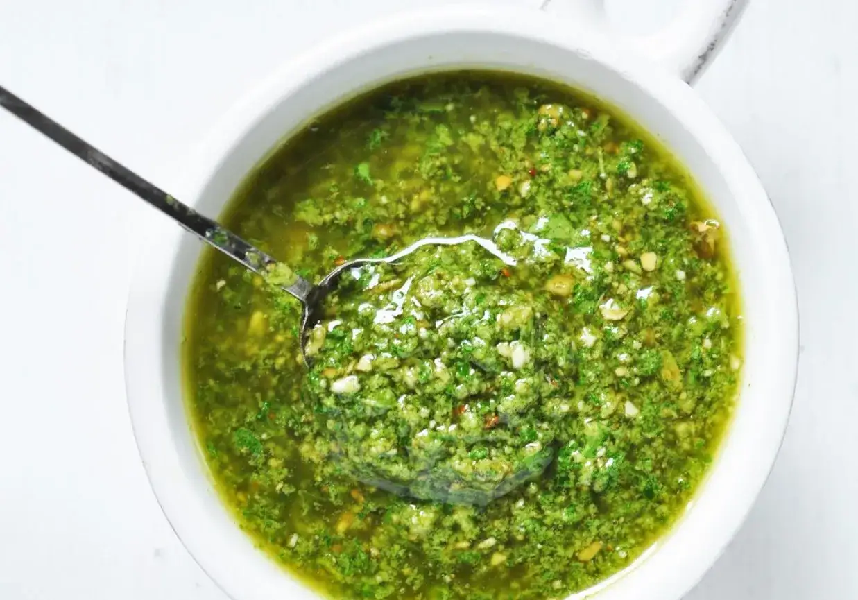 Pesto z rukoli w białej misce, z łyżką pełną aromatycznego sosu. Idealne do makaronu.
