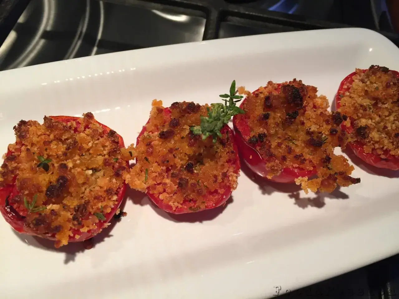 Pomodori gratinati al forno, ripieni di pangrattato e erbe aromatiche, serviti su un piatto bianco.