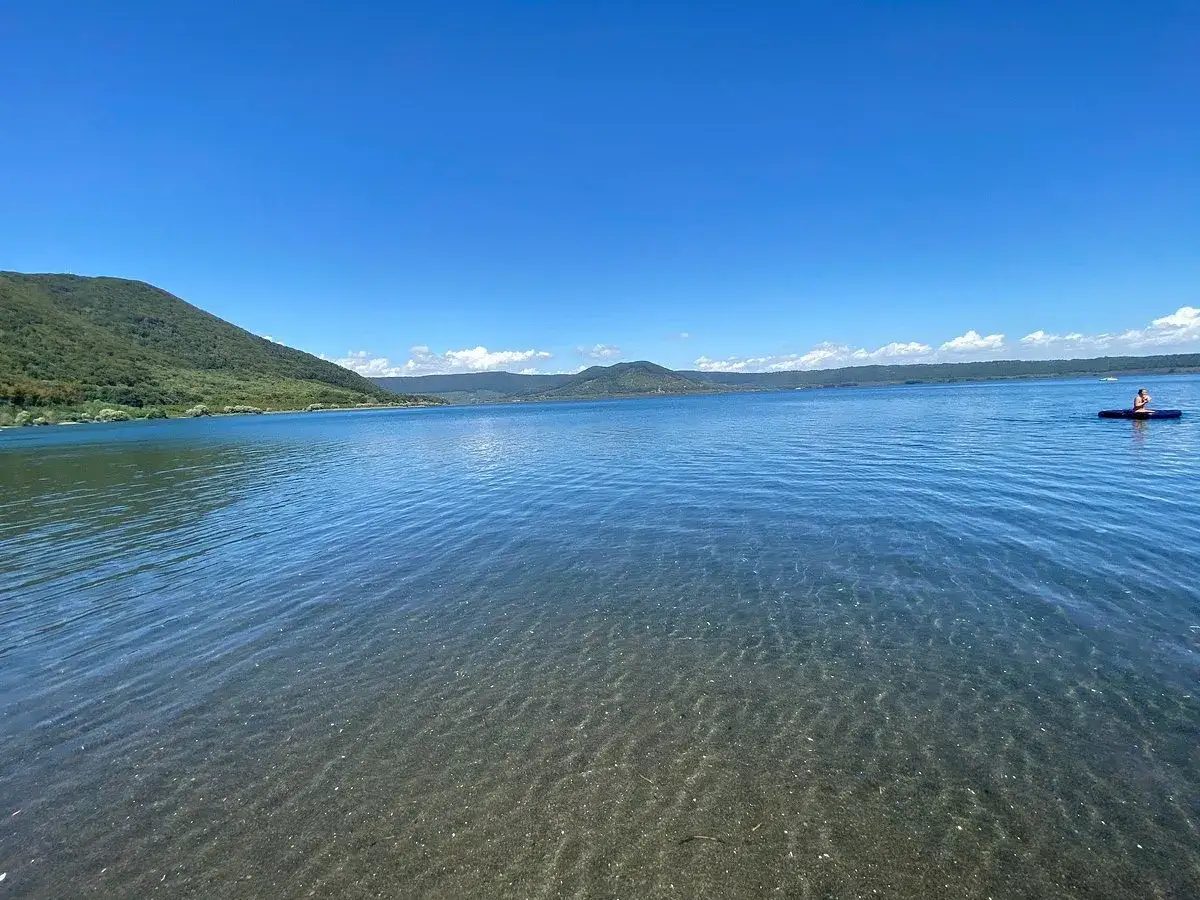 Un uomo in paddleboard solca le acque limpide del lago di Vico, circondato da colline verdi sotto un cielo azzurro.