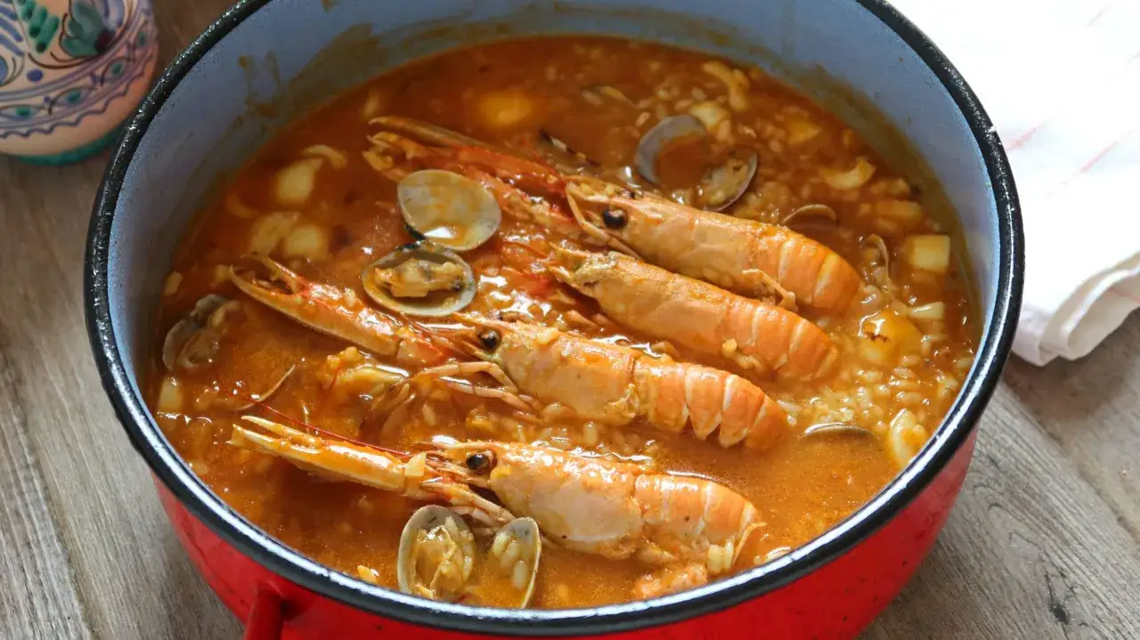 Un delicioso arroz caldoso con gambas y almejas, servido en una cazuela roja.