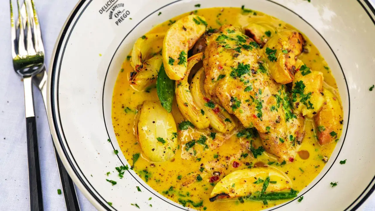 Kyckling i kr&auml;mig, gul s&aring;s med gr&ouml;nsaker, liknande tikka masala, serverad p&aring; en tallrik med en gaffel bredvid.