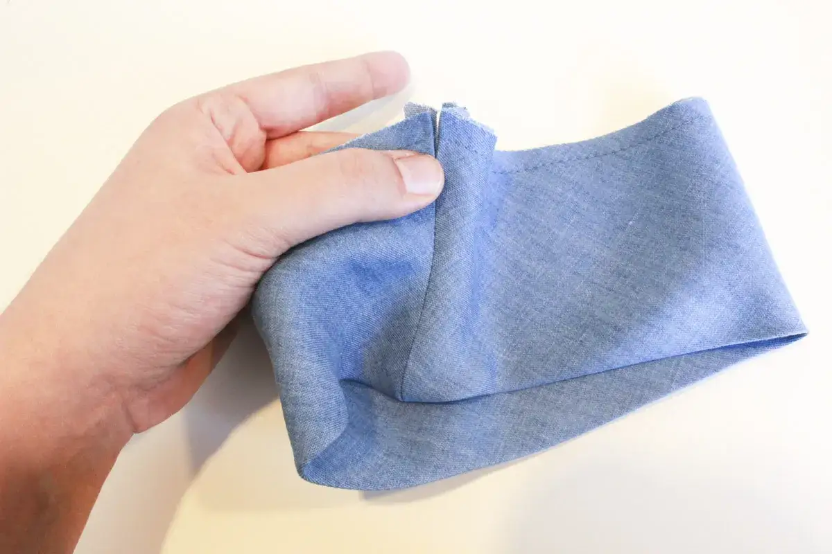 A hand demonstrates how to sew a folded cuff band to a sleeve, showing the fabric edge being prepared for stitching.