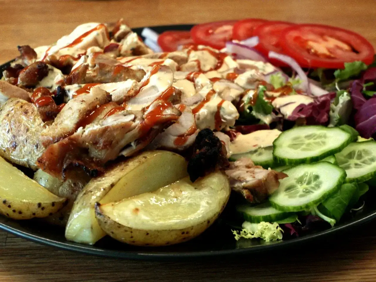 En tallrik med kyckling kebab, potatisklyftor, sallad, gurka och tomater. En härlig måltid!