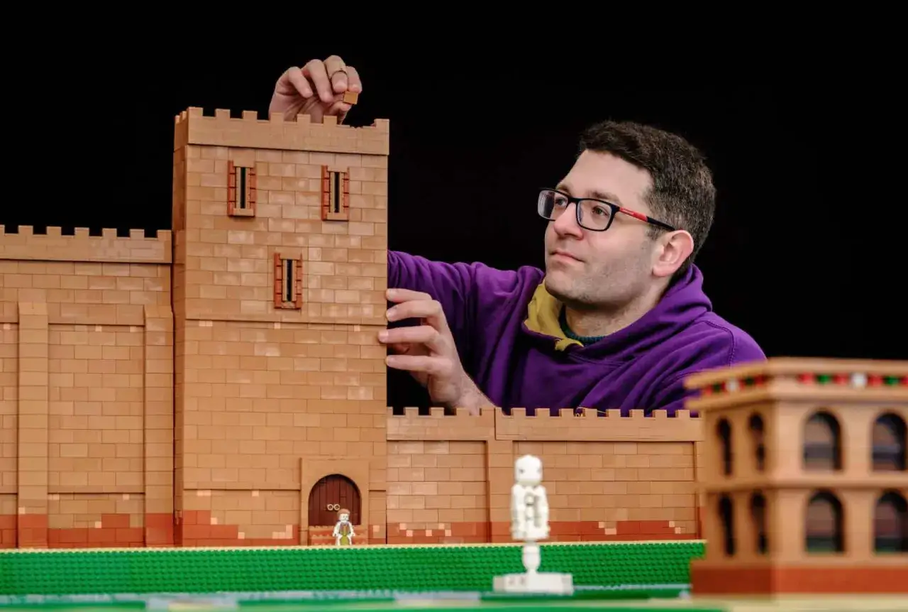 Ein Mann baut eine beeindruckende LEGO-Burg, ein wahres MOC (My Own Creation). Kleine Figuren und ein weiteres Geb&auml;ude sind bereits Teil der Szene.