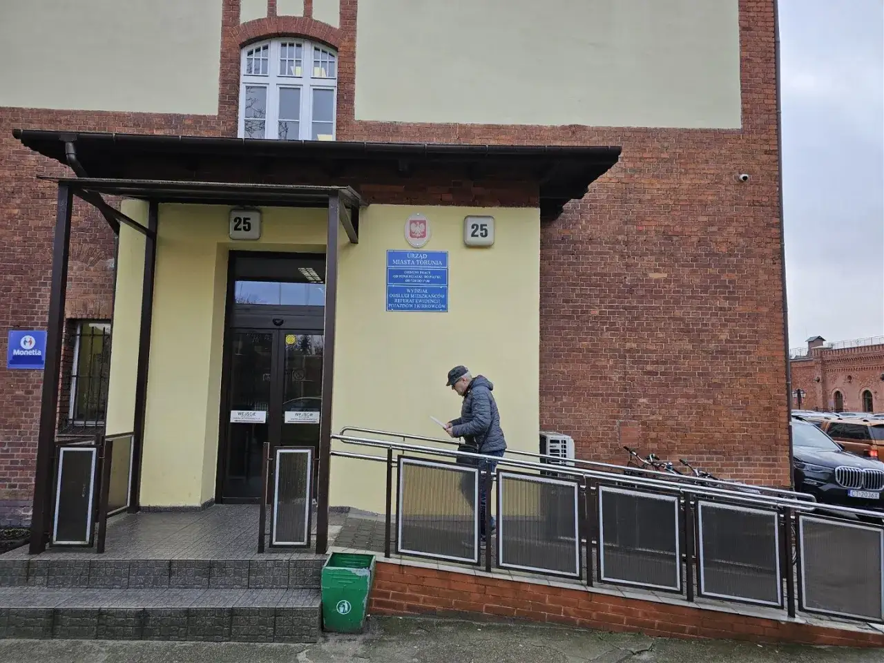 Mężczyzna idzie po rampie do budynku urzędu miasta, gdzie dokonuje się rejestracja pojazdów.