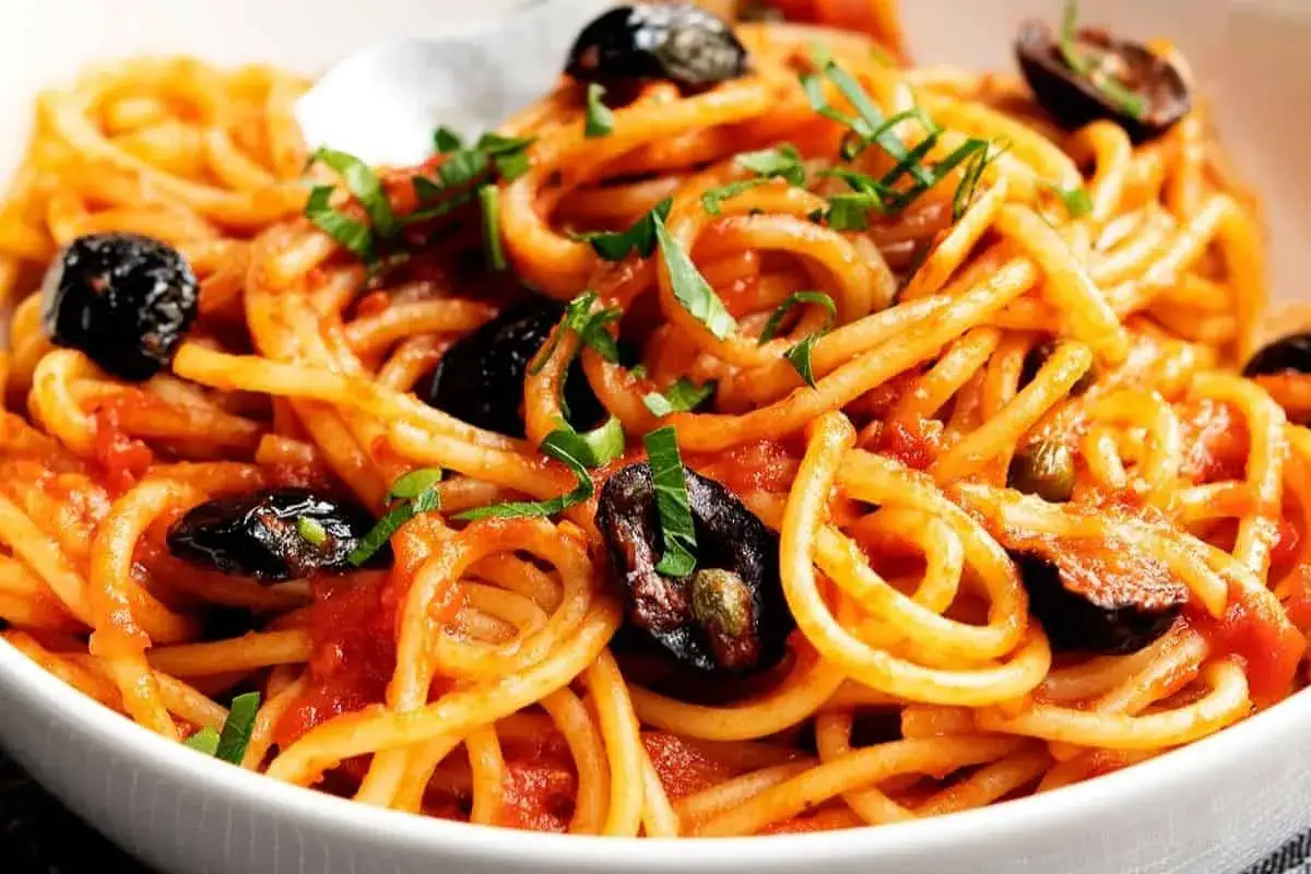 Ein Teller Spaghetti Puttanesca mit schwarzen Oliven und Kapern, garniert mit frischer Petersilie.