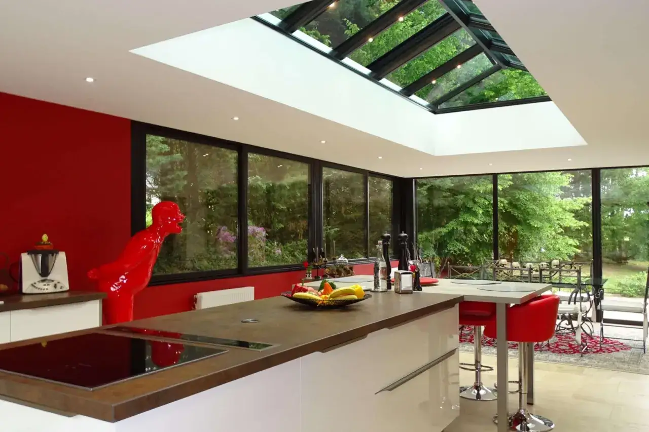 Cuisine moderne avec une **veranda puit de lumiere** baign&eacute;e de soleil, murs rouges, &icirc;lot central et sculpture audacieuse.