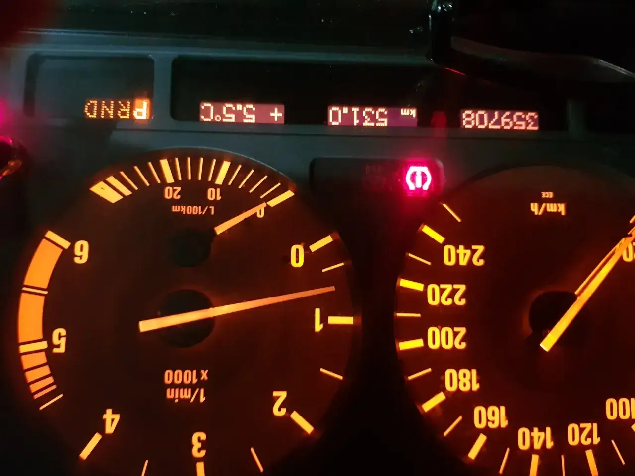 Czerwony wykrzyknik BMW świeci się na desce rozdzielczej, obok wskaźników prędkości i obrotów.
