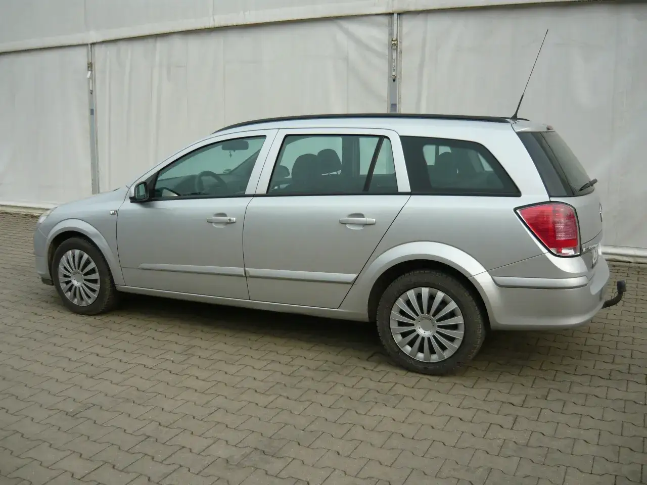 Srebrny Opel Astra 2005 kombi stoi na kostce brukowej.