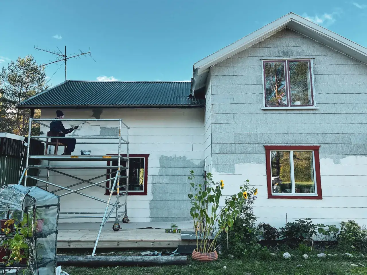 Person målar om husets eternit fasad från ställning.
