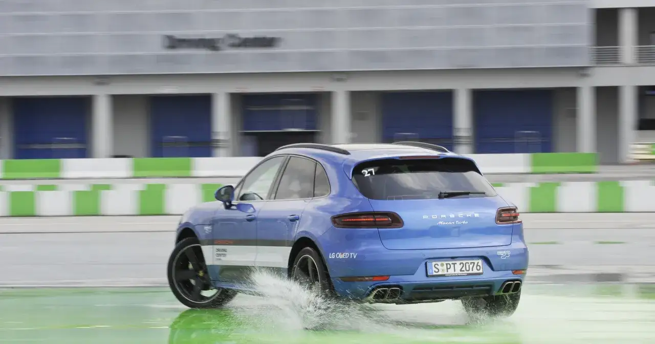 Niebieski Porsche Macan Turbo na mokrym torze, rozpryskuje wodę. DSC co to? To system stabilizacji, który pomaga w takich sytuacjach.