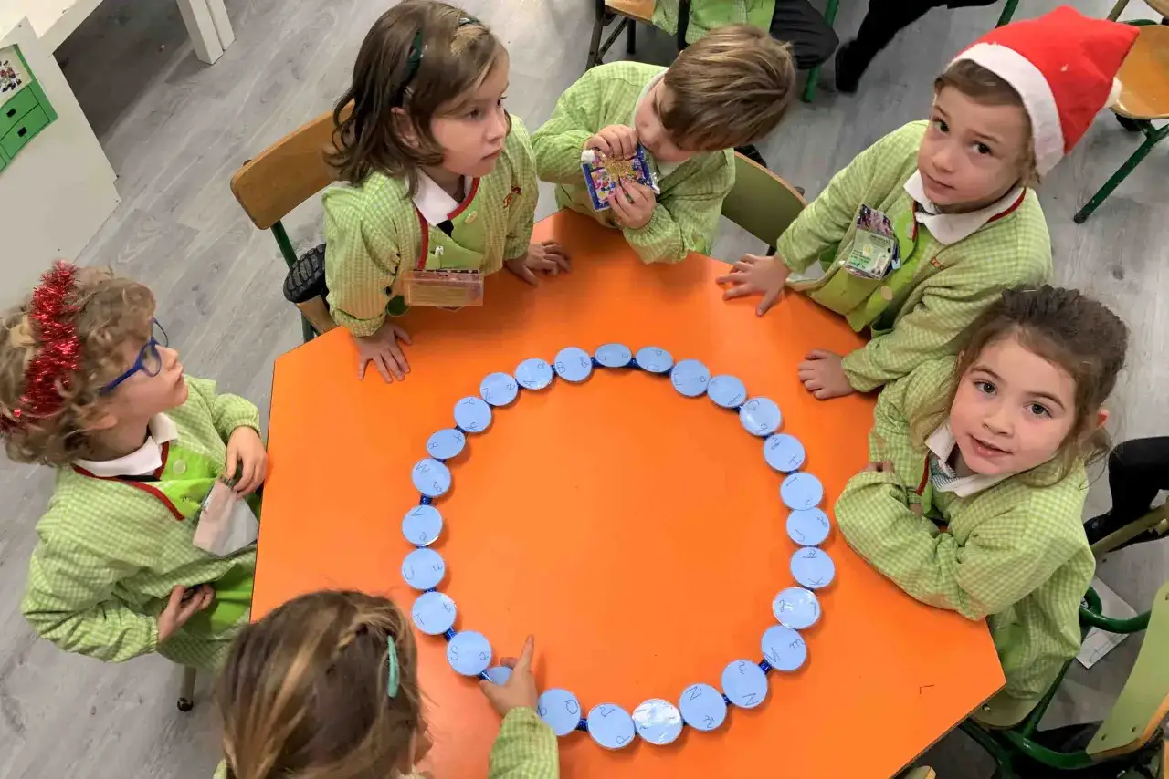 Niños juegan al pasapalabra navidad con un círculo de letras azules en una mesa naranja.