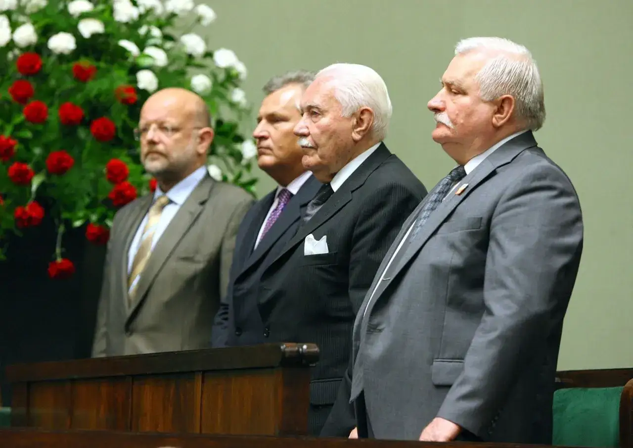 Czterech mężczyzn w garniturach, w tym Lech Wałęsa, stoi przed bukietem kwiatów. Czy to symbolizuje, dlaczego urząd prezydenta traci na znaczeniu w systemie kanclerskim projektowanym przez rząd?