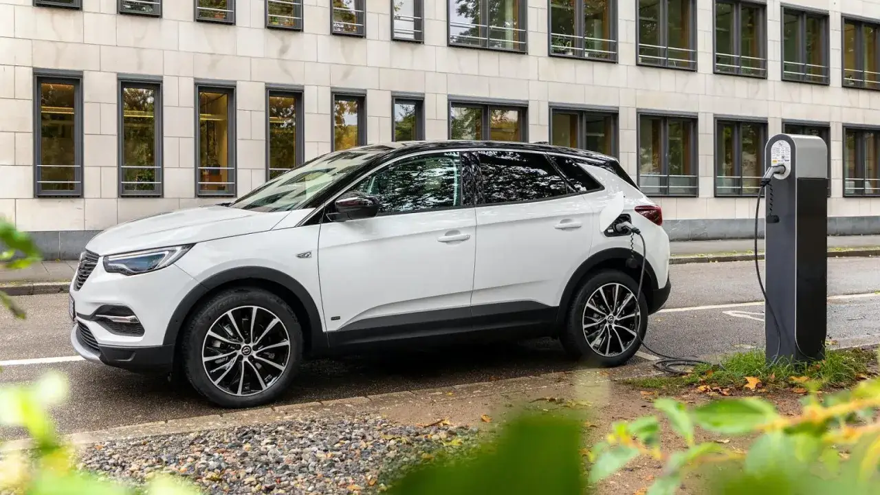 Biały Opel Grandland ładuje się przy stacji. Sprawdź aktualną opel grandland cena i wybierz swój nowy samochód.