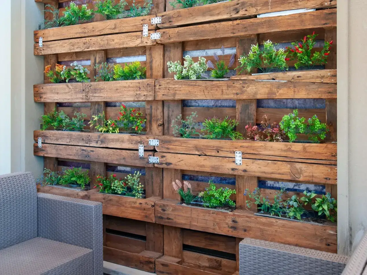Un **jardín vertical con palets** exhibe plantas verdes y rojas en compartimentos de madera rústica, creando un oasis natural.