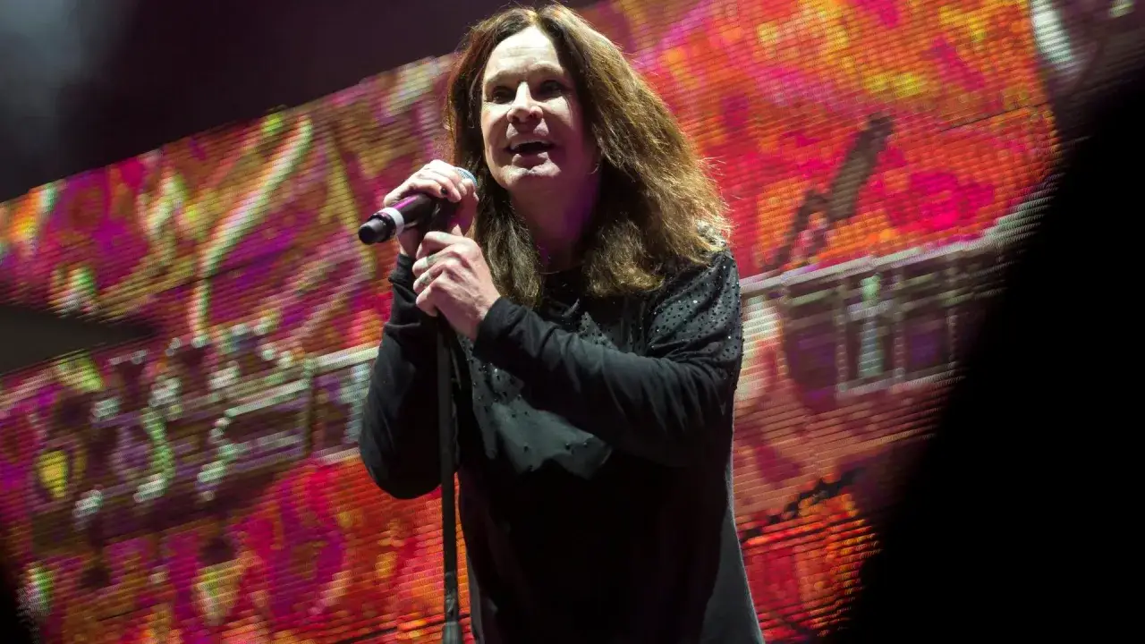 Ozzy Osbourne śpiewa na koncercie, trzymając mikrofon. Tło to kolorowy ekran z abstrakcyjnym wzorem.