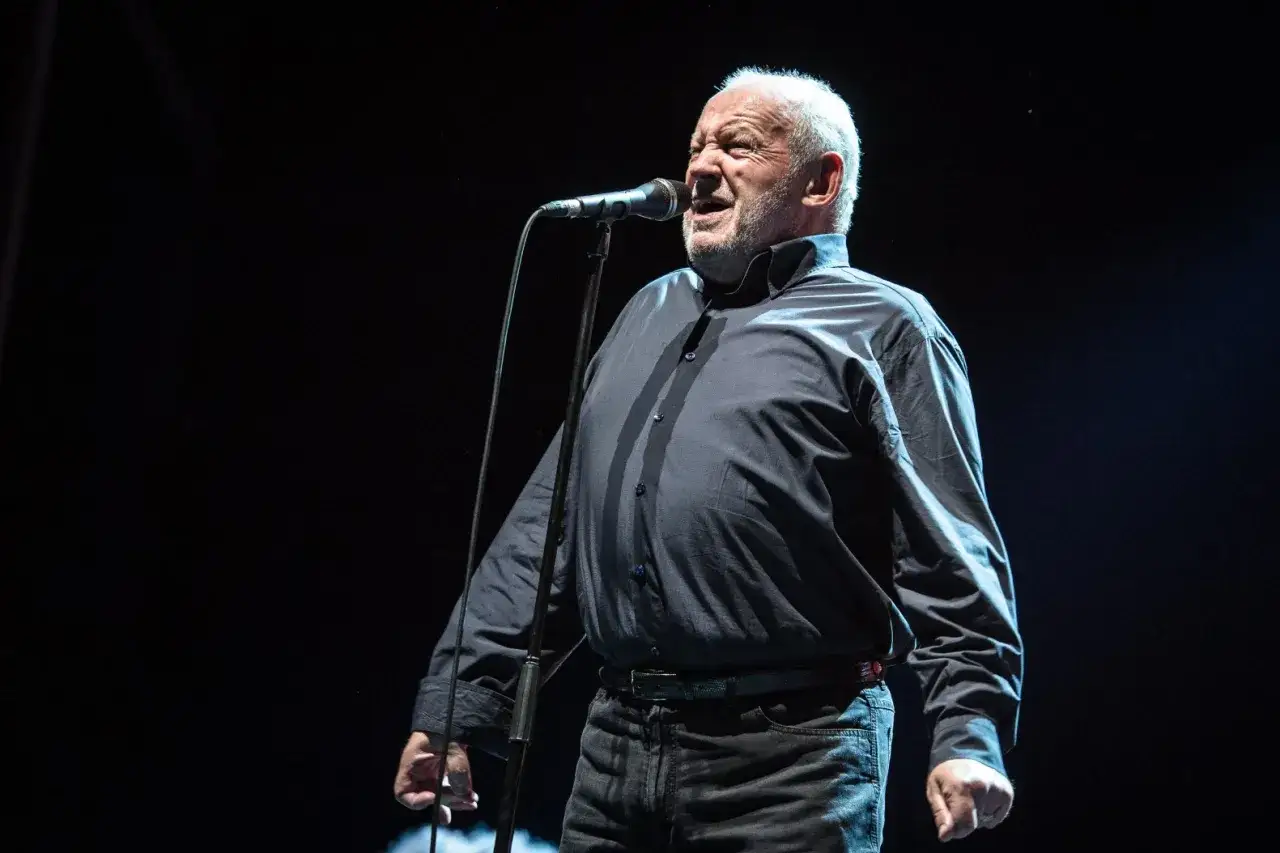 Joe Cocker śpiewa na scenie, wykonując swoje niezapomniane utwory.