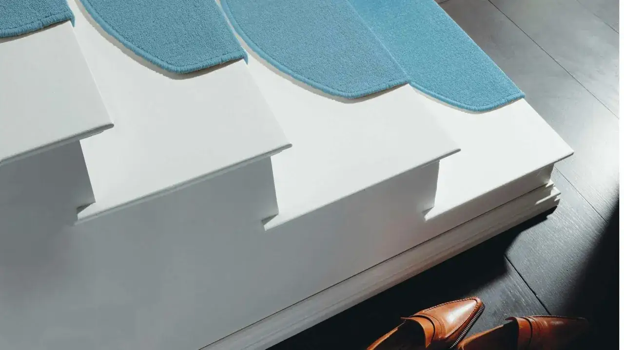 Moderne Treppe mit blauen Teppichl&auml;ufern, die eine Beton-Treppe verkleiden. Elegante Lederschuhe liegen daneben.