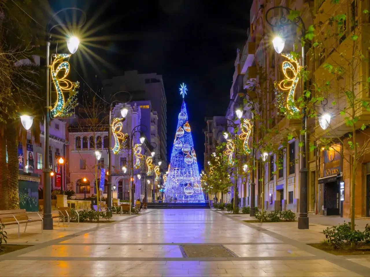 Ulica ozdobiona świątecznymi iluminacjami, z ogromną choinką w tle. Idealne miejsce na Sylwestra, a może nawet tanie loty na Sylwestra?