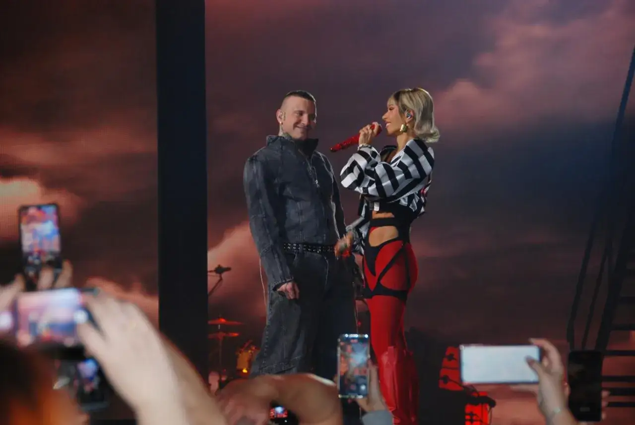 Hania Rani na scenie, w czerwonych legginsach i czarno-białej bluzce, śpiewa do mikrofonu. Obok niej stoi mężczyzna w dżinsowej kurtce.