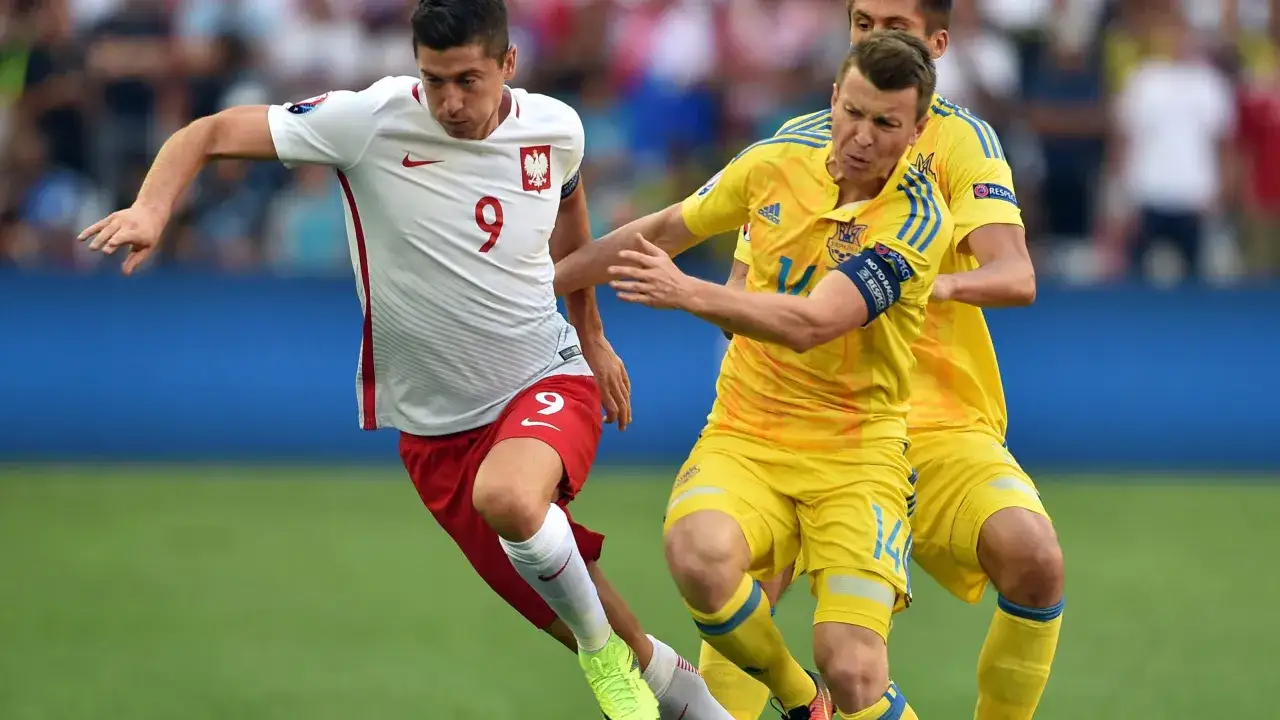 Piłkarz Polski z numerem 9 walczy o piłkę z zawodnikiem Ukrainy. Emocje na boisku podczas meczu euro Polska Ukraina.
