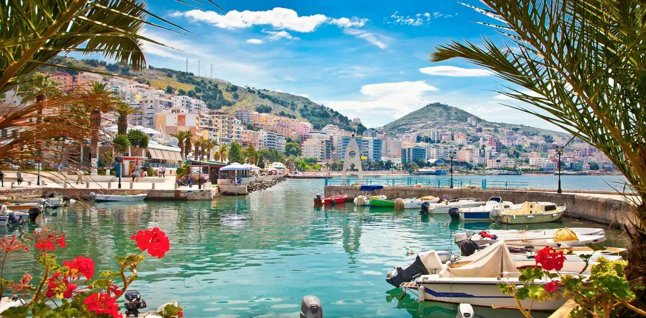 Bunte H&auml;user am Hang, Boote im t&uuml;rkisfarbenen Wasser &ndash; ein malerischer Ort, wo in Albanien Urlaub machen Spa&szlig; macht.