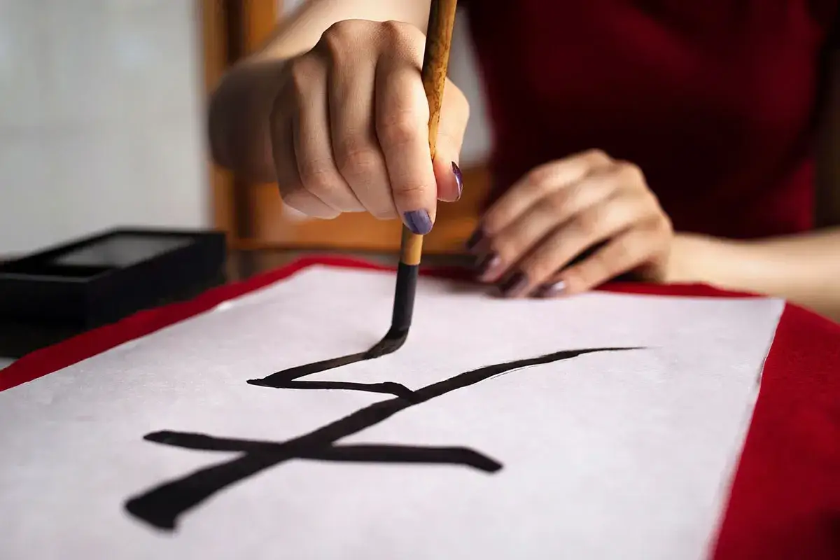 Une main crée la calligraphie chinoise sur du papier blanc, le pinceau trempé dans l'encre noire.