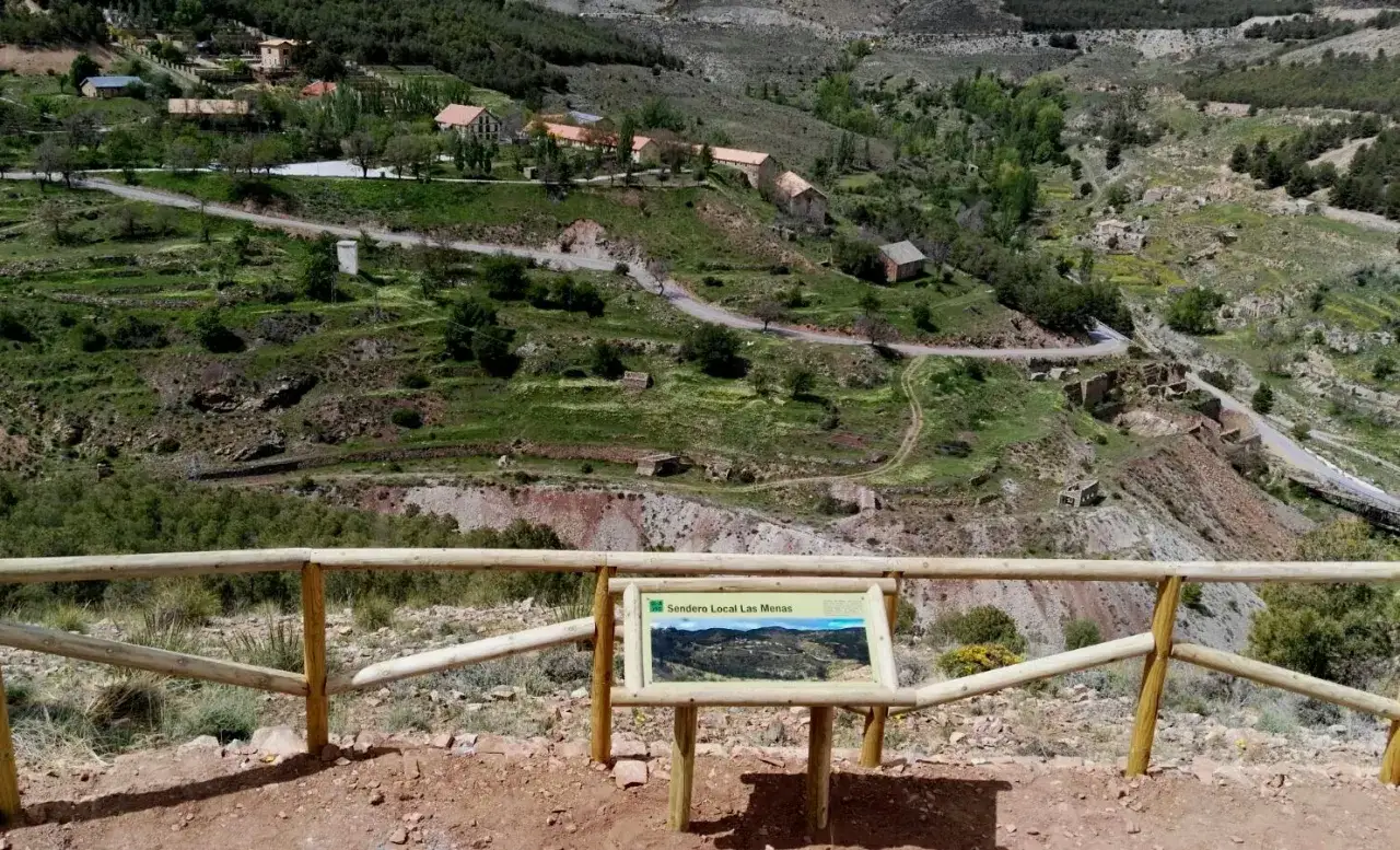 Sendero Local Las Menas: un paisaje monta&ntilde;oso con casas dispersas y ruinas, evocando la historia de las menas.
