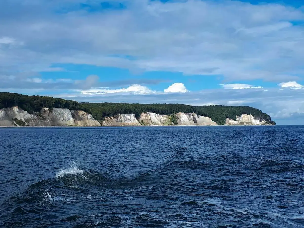 Kreidefelsen bei Sassnitz an der Ostsee, mit tiefblauem Meer und bewaldeter Klippenlinie unter einem Wolkenhimmel.
