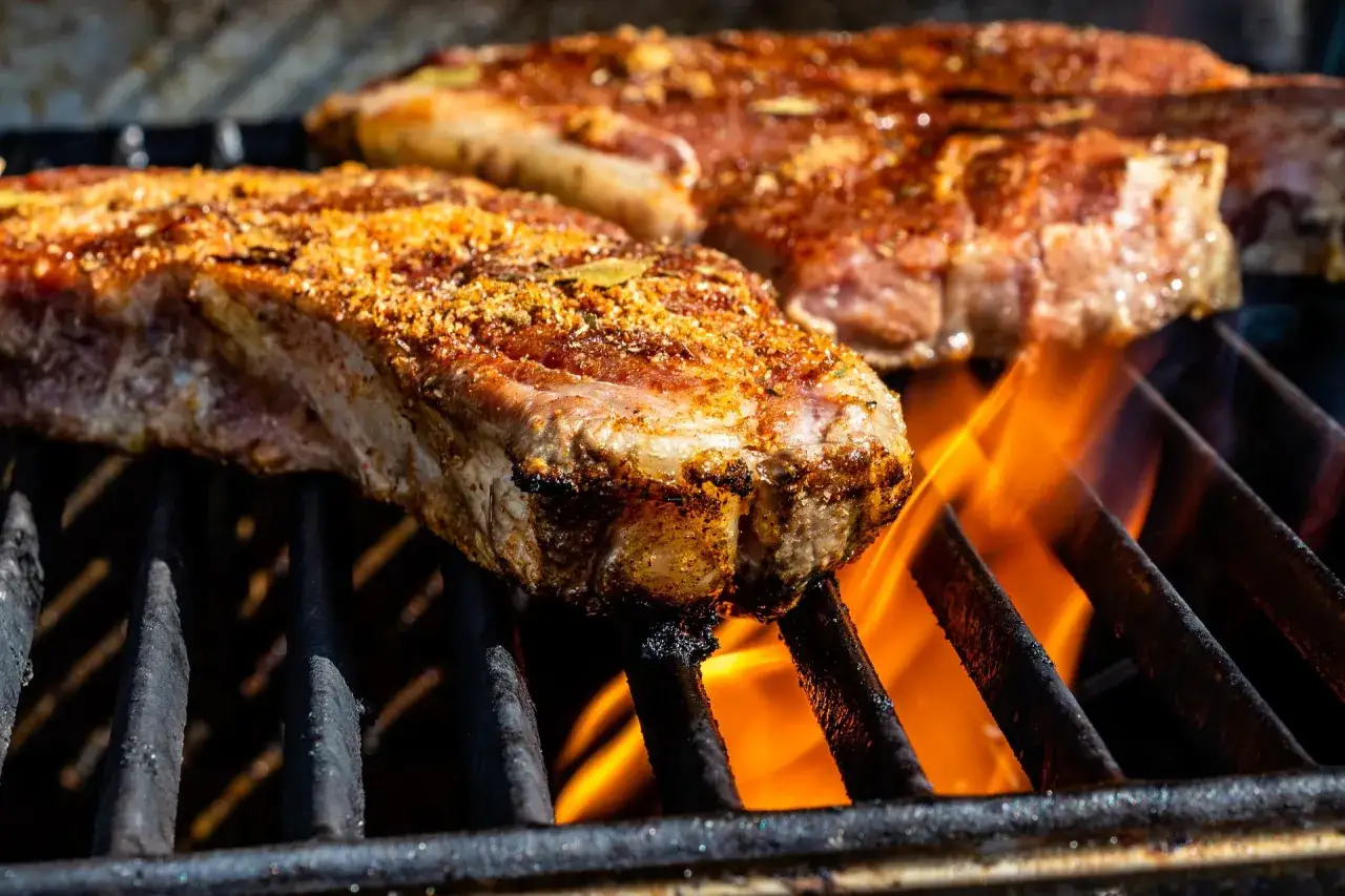 Deux entrecôtes savoureuses en cuisson sur un barbecue, les flammes dansent sous la viande.