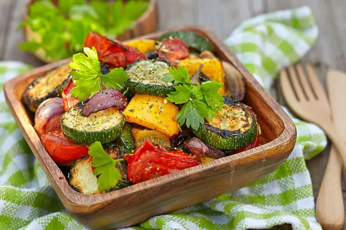 Verdure miste cotte in friggitrice ad aria: zucchine, peperoni, pomodori e cipolle, condite con erbe aromatiche e servite in una ciotola di legno.