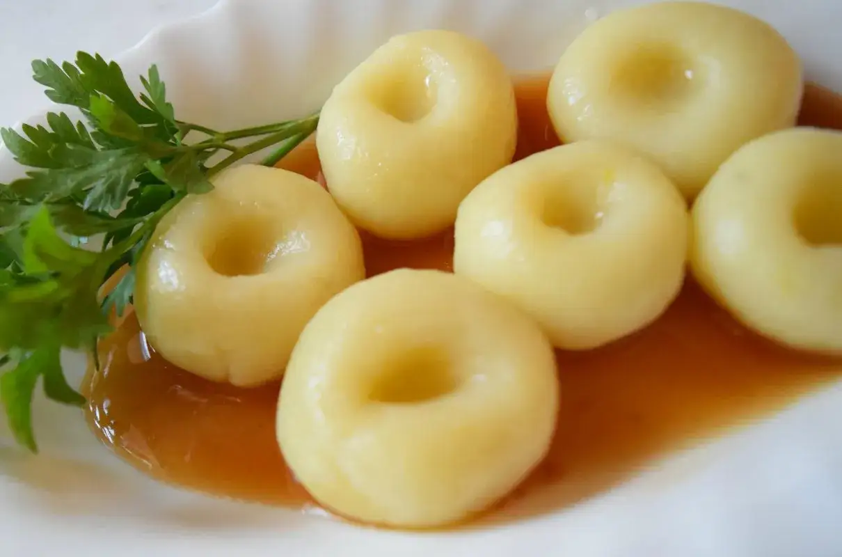 Pyszne, domowe kluski śląskie, czyli makaron gnocchi, polane sosem i udekorowane natką pietruszki.