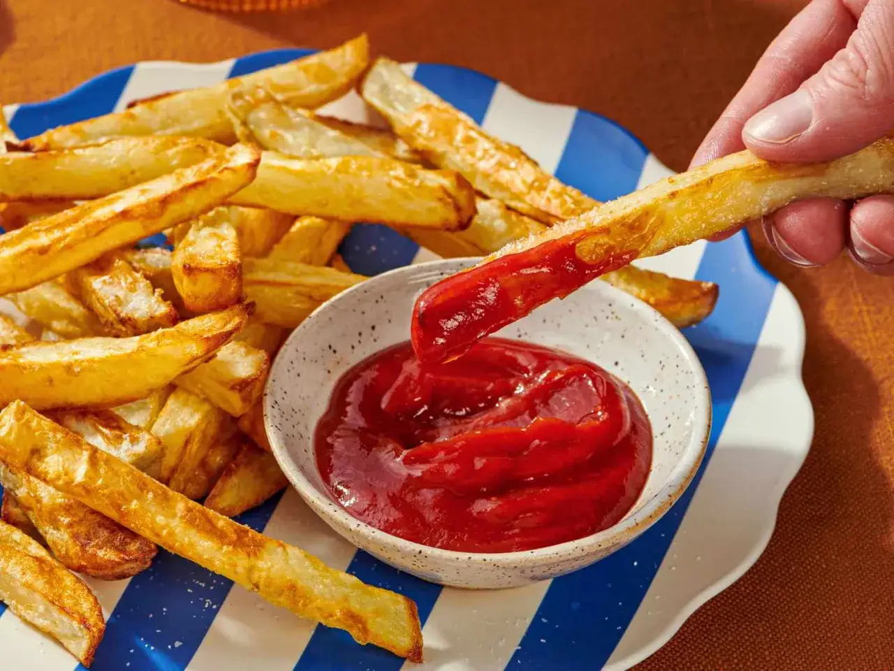 Chrupiące frytki z airfryer zanurzane w keczupie. Idealna przekąska na każdą okazję.