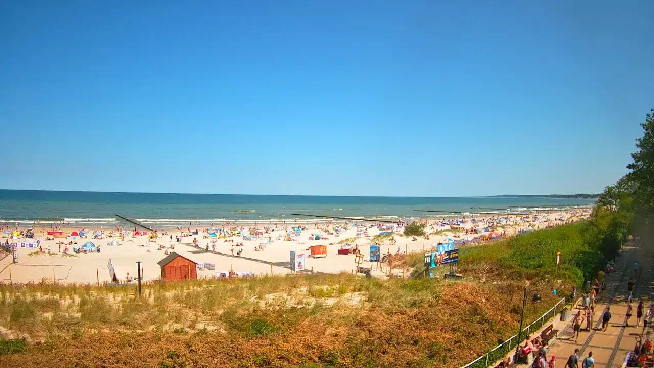 Słoneczny dzień na plaży, kąpielisko u ujścia Słupi do Bałtyku. Tłumy plażowiczów, parasole i budki ratownicze.