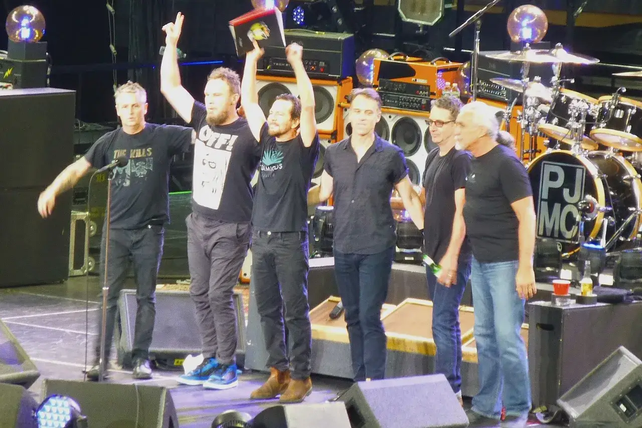 Les membres de Pearl Jam sur scène, certains tenant des objets, avec des amplis et une batterie en arrière-plan.