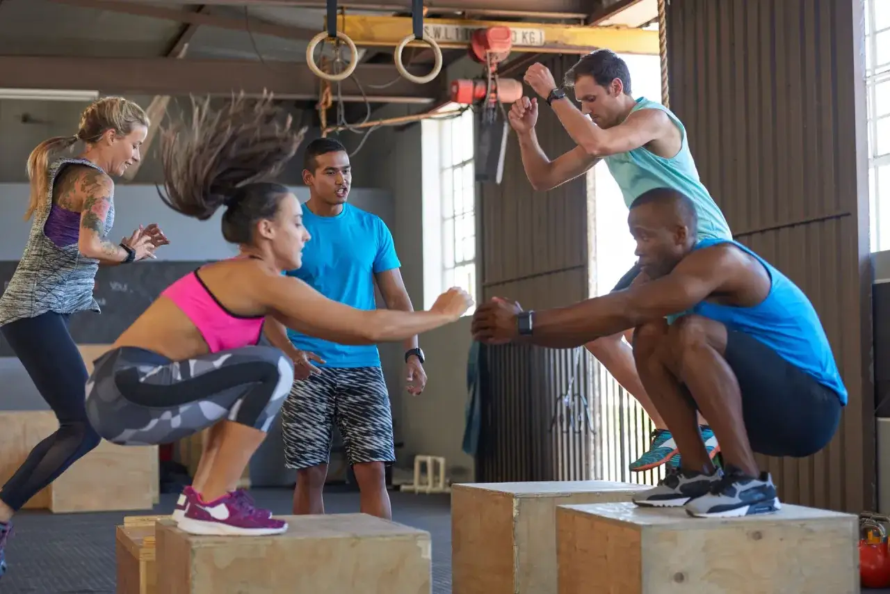 Grupa ludzi ćwiczy czym jest crossfit, wykonując skoki na skrzynie w sali treningowej.