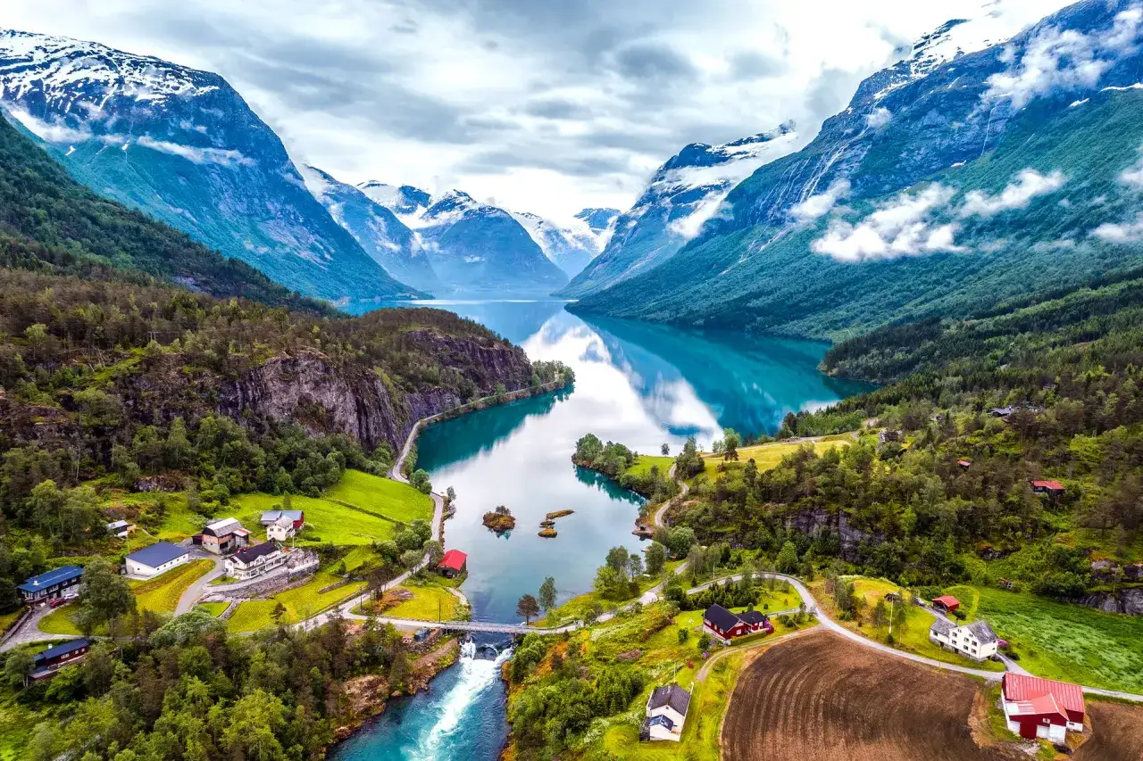 Malowniczy widok na fiord i góry, idealny na wycieczki do Norwegii. Domy wtopione w zieleń, odbijające się w turkusowej wodzie.